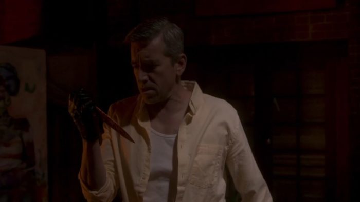 A man looks at a bloody knife in his gloved hand in Tales from the Other Side