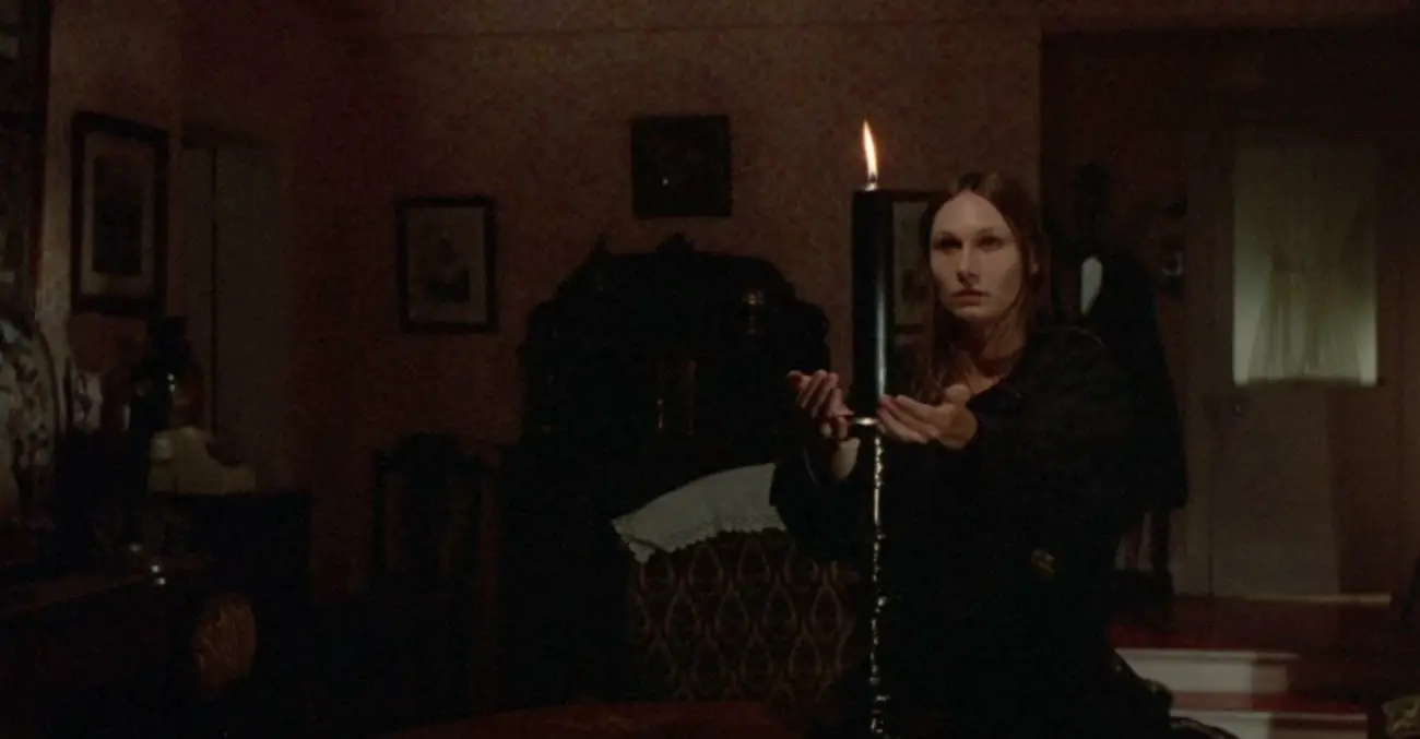 A woman standing behind a candle with her hands out, focused.