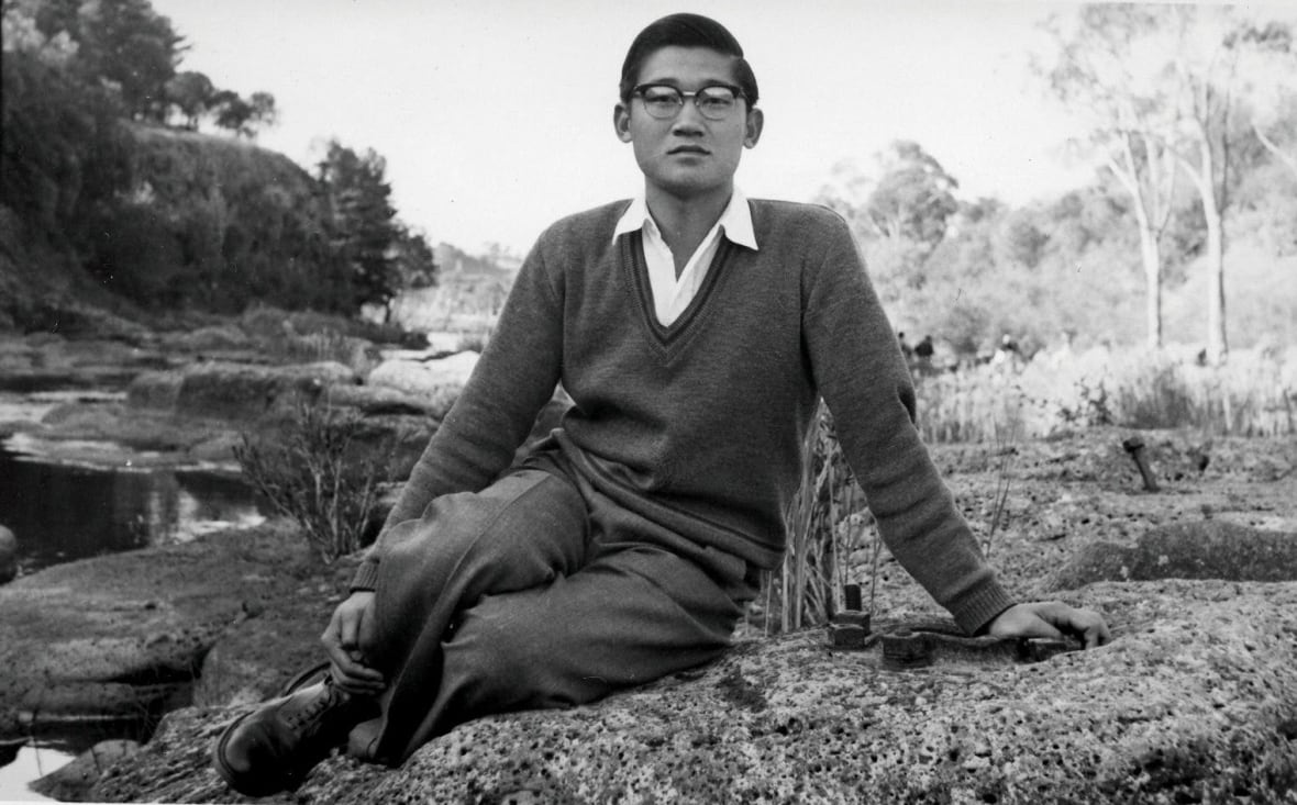 A black and white photo of an Asian man wearing glasses. 