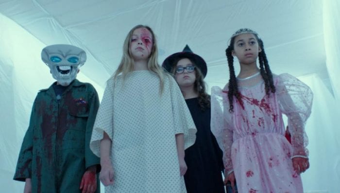 A group of blood covered trick or treaters stand in a room covered in plastic sheets.